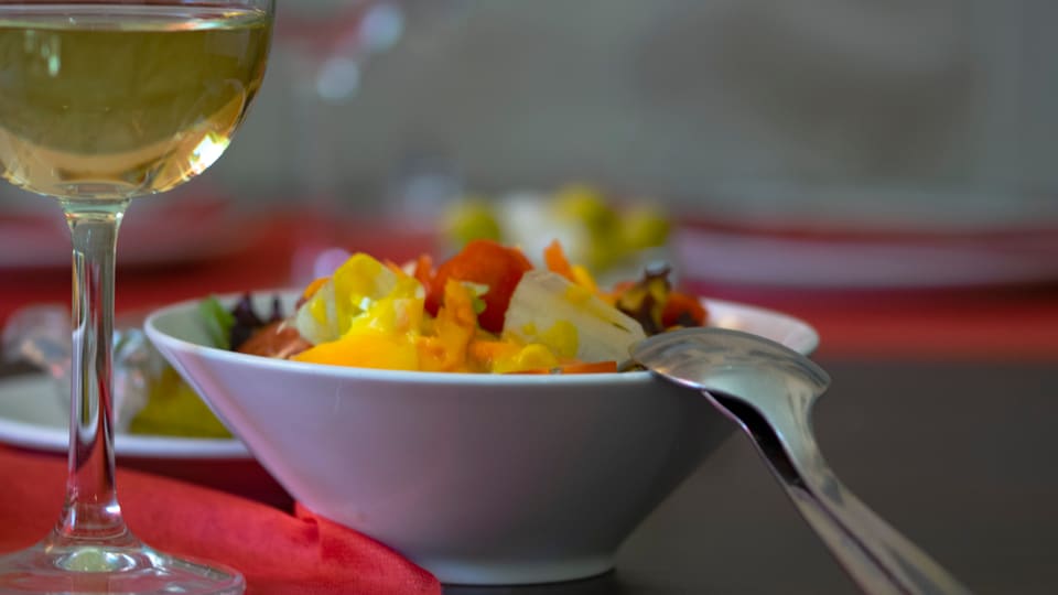 Salad and a glass of white wine on a table with a red tablecloth