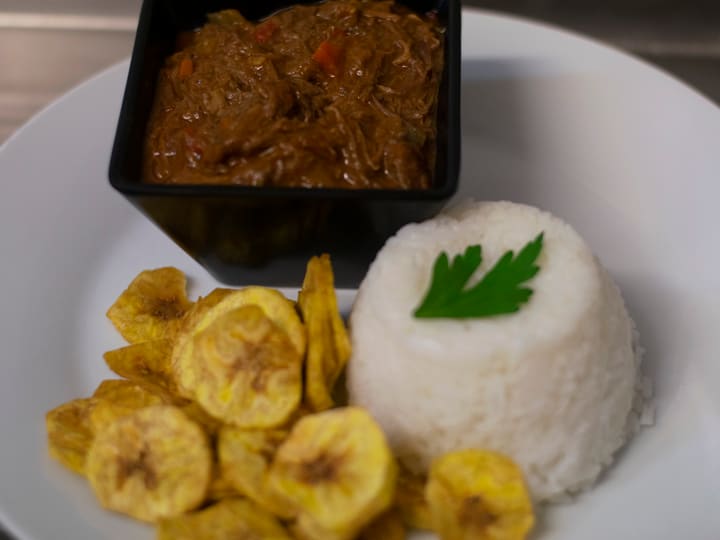 Ropa vieja with white rice and plantain chips on a red tablecloth